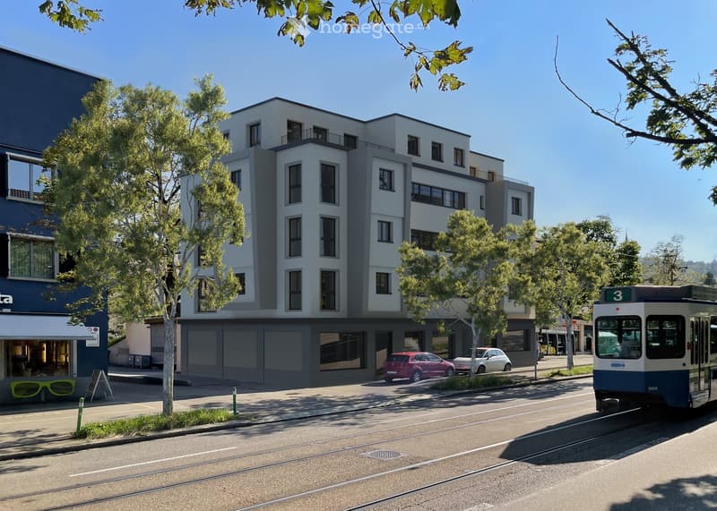 Modern multi-story building with large windows and balconies, surrounded by trees and parked cars, with a tram passing by on the street.