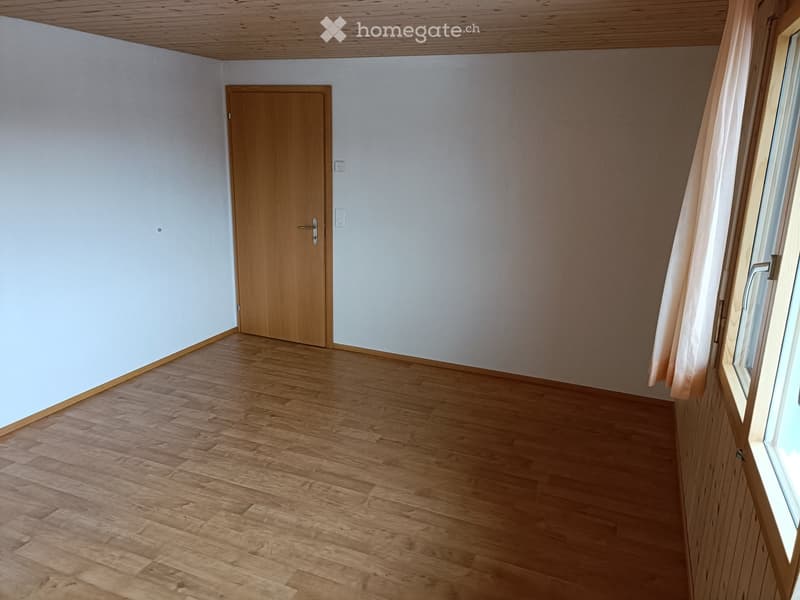 Empty room with light wooden flooring, white walls, a wooden door, and a window with a curtain.