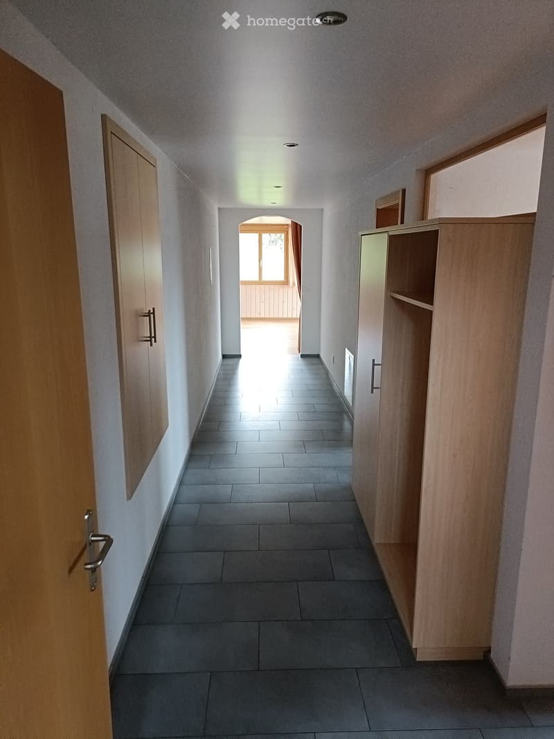 Clean, well-lit hallway with tiled floor, wooden doors, and built-in wooden shelving unit on one side.