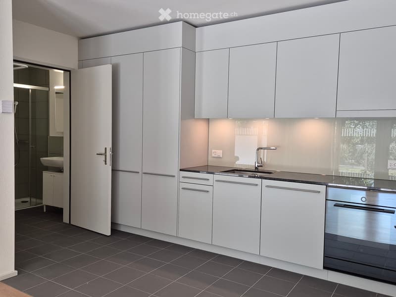Modern kitchen with white cabinets, dark tiled floor, stainless steel sink, and built-in oven.