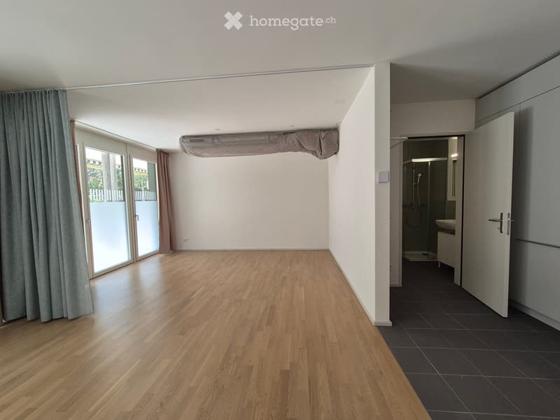 Empty room with wooden flooring, large sliding glass doors leading to a balcony, and an adjacent bathroom with tiled flooring.