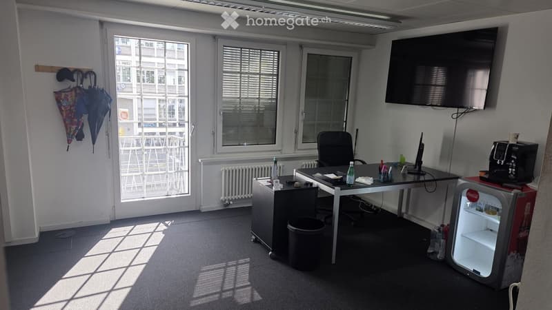 Office space with a desk, chair, screen, refrigerator, and umbrella on the wall.