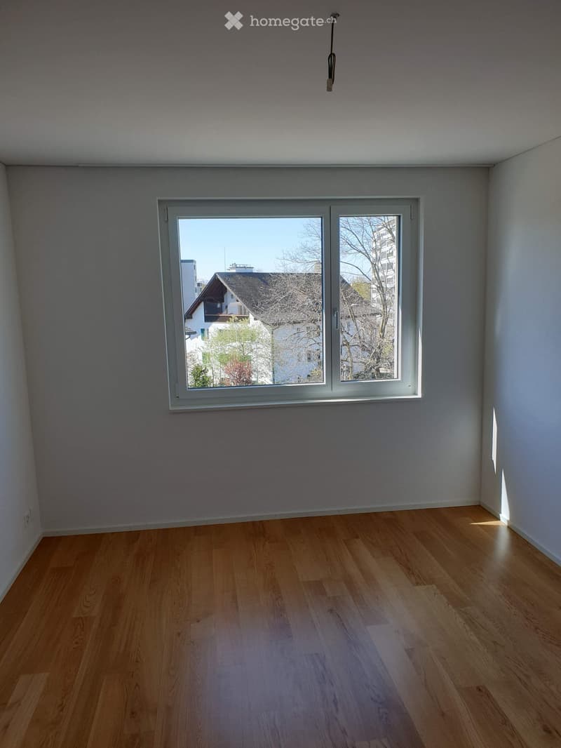 Empty room with wooden flooring and large window showing outdoor view.