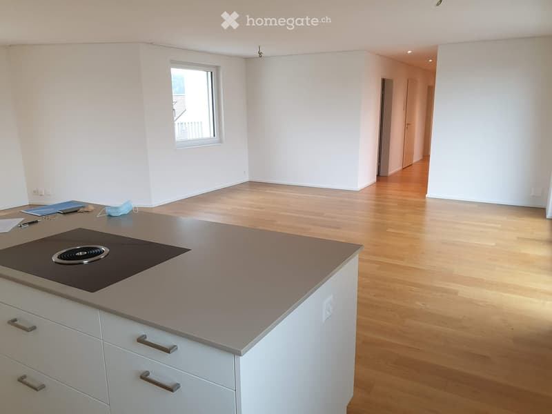 Modern kitchen with white cabinets, a central island, and an induction stove. The floor is light wooden, and there is a window with a view of a balcony.