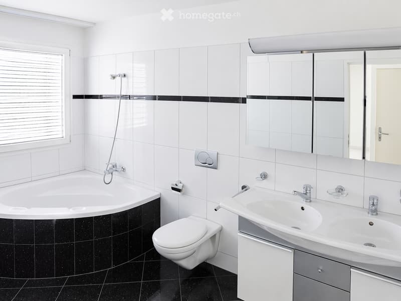 Modern bathroom with white tiles, black accents, bathtub, toilet, double sink, and large mirror.