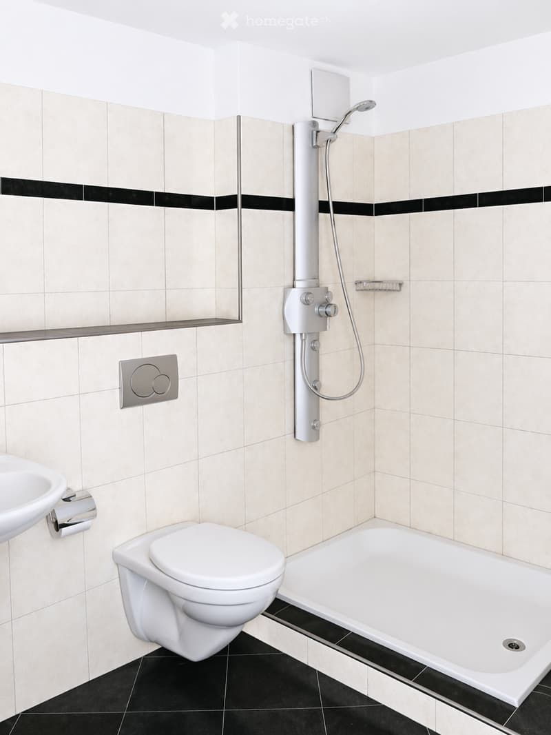 Modern bathroom with beige tiled walls, black accents, a bathtub, toilet, sink, and a handheld showerhead.