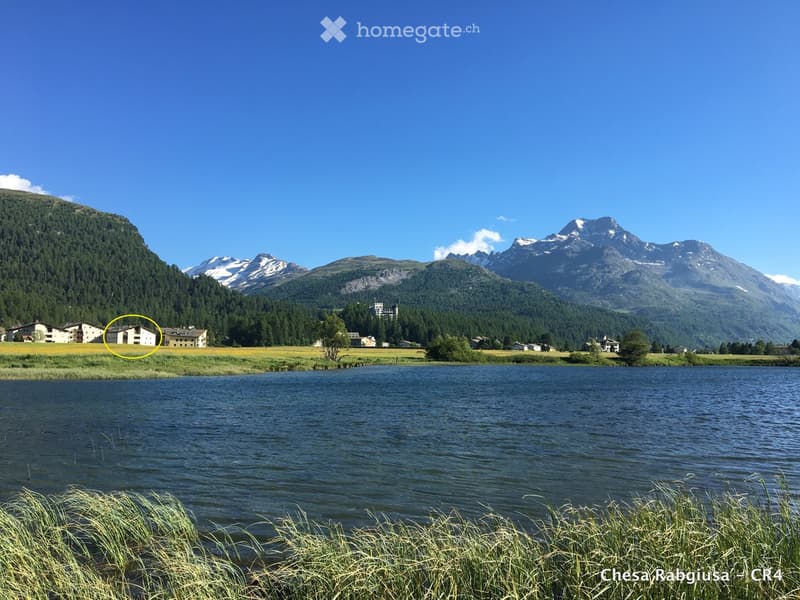 Scenic view of a lake surrounded by mountains, with a small cluster of buildings on the shore.