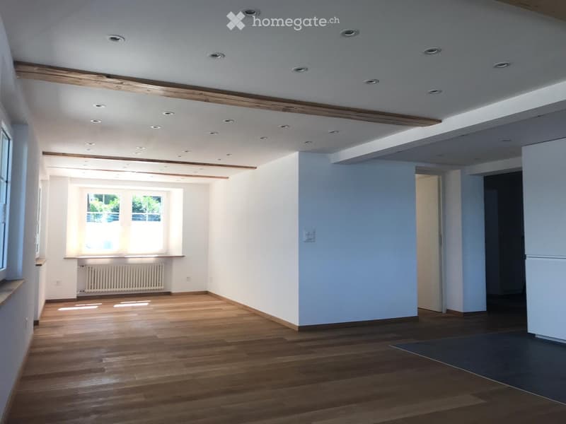 Empty room with wooden flooring, white walls, and recessed ceiling lights. Features large windows and a radiator under one window.