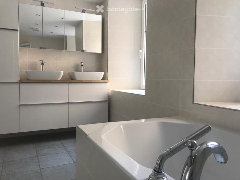 Modern bathroom with a bathtub, two sinks, a large mirror, and a window with floral-patterned tiles.