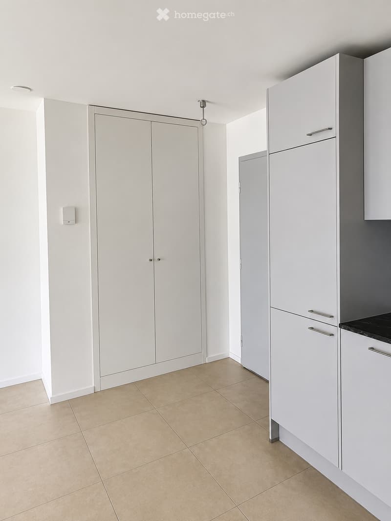 Empty room with white walls, beige tiled floor, and built-in white cabinets with silver handles.