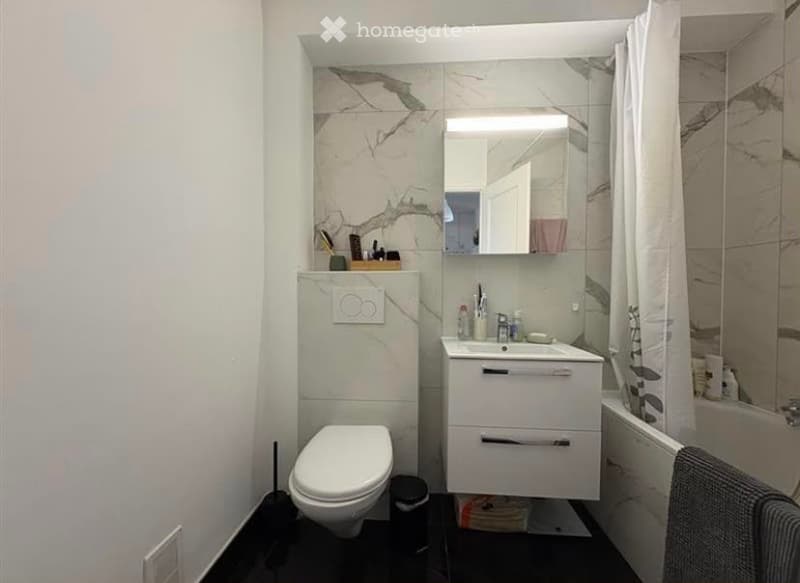 Modern bathroom with white marble tiles, a toilet, a sink with a mirror, and a shower area with a curtain.