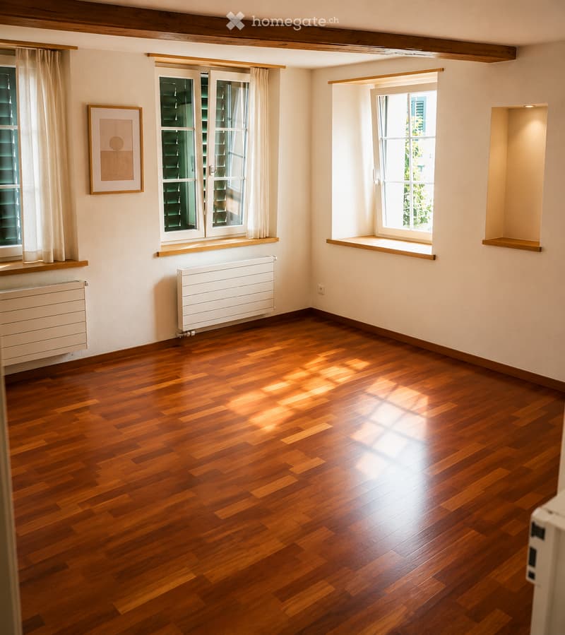 Empty room with wooden flooring, white walls, large windows with curtains, radiators, and a framed picture on the wall.