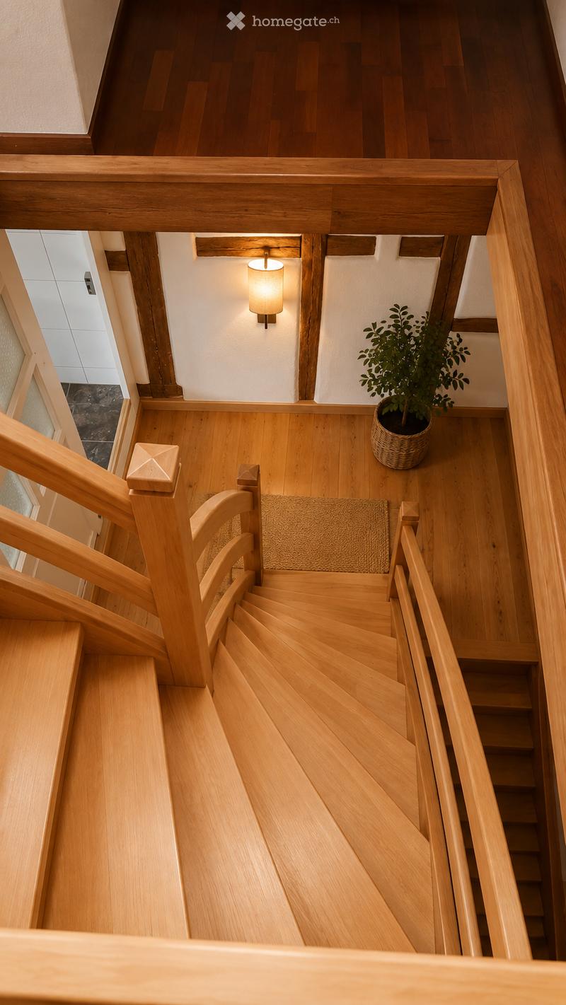 Spiral staircase with wooden steps and handrails, a wall-mounted light fixture, a potted plant, and a small rug on the landing.