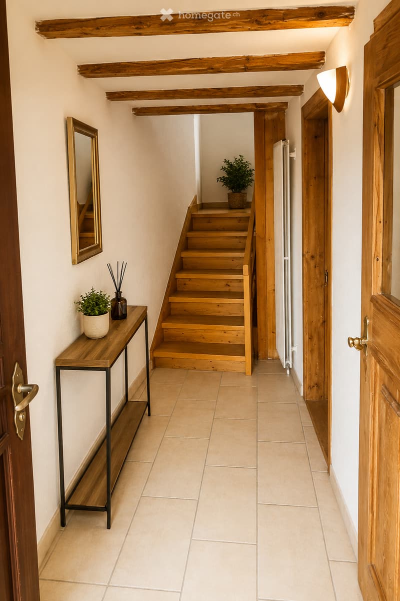 A well-lit hallway with wooden beams on the ceiling, a small wooden table with a potted plant and decorative items, a staircase leading upwards, and a mirror on the wall.