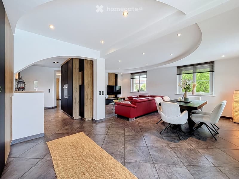 Modern living and dining area with a red sofa, dining table with chairs, television, and kitchen cabinet visible.