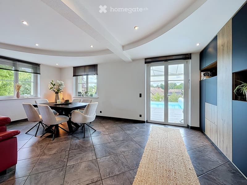 Modern dining area with a dark wooden table, white chairs, a red sofa, and a large sliding glass door leading to a pool area.