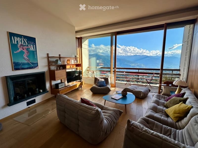 Modern living room with large windows offering a mountain view, a fireplace, a sofa, a coffee table, and a TV stand.