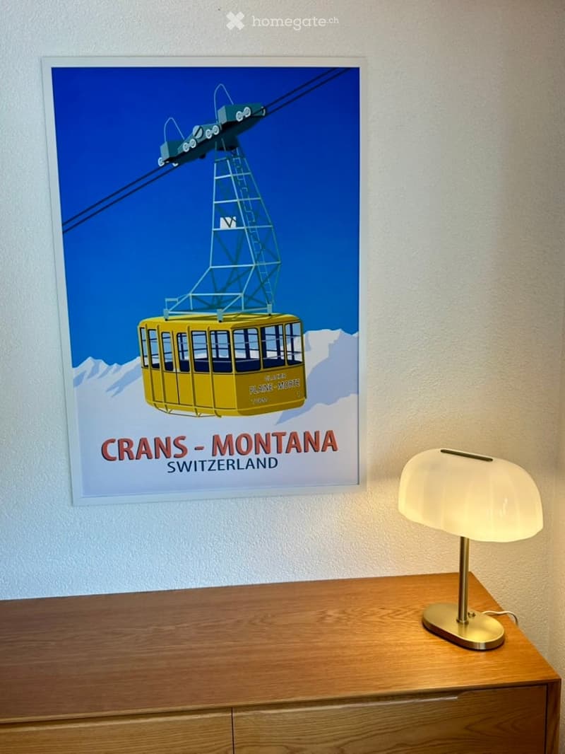 A wooden table with a modern lamp and a large poster of a cable car on the wall.