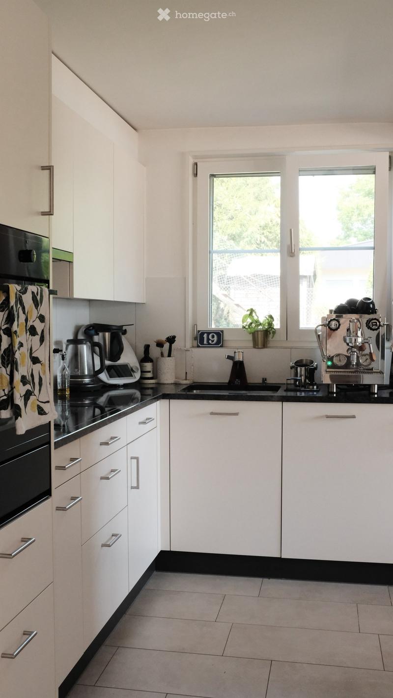Modern kitchen with white cabinets, black countertops, and stainless steel appliances including an oven, coffee maker, and sink.