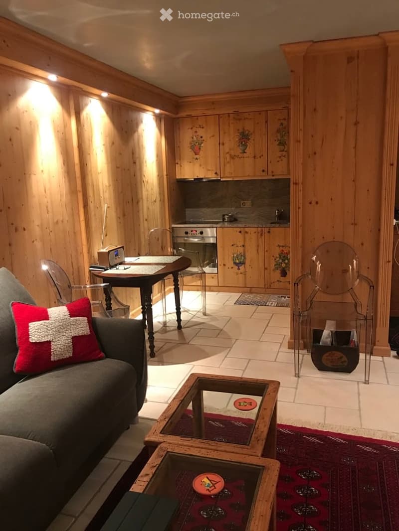 A cozy, wood-paneled living and dining area with a sofa, coffee table, dining table, chairs, and a small kitchen area with cabinets and an oven.