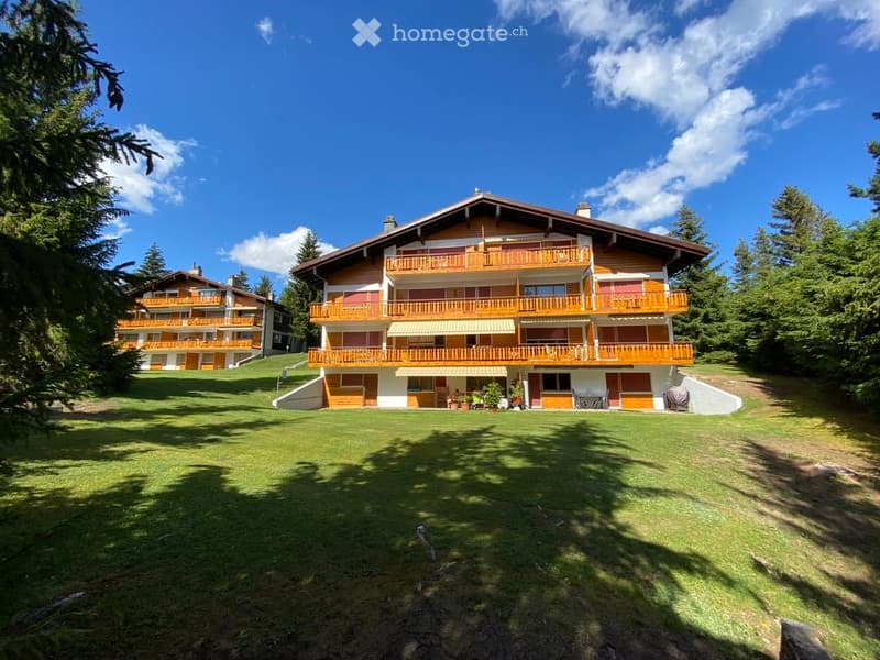 A large, multi-story wooden building with balconies and a well-maintained lawn in a forested area.