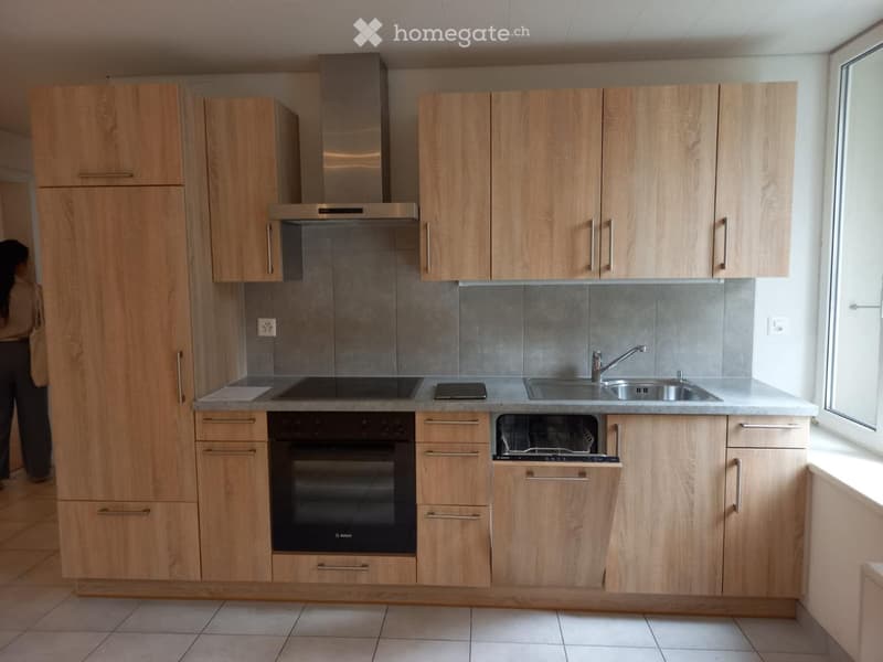 Modern kitchen with light wood cabinets, stainless steel appliances, and a grey tiled backsplash.