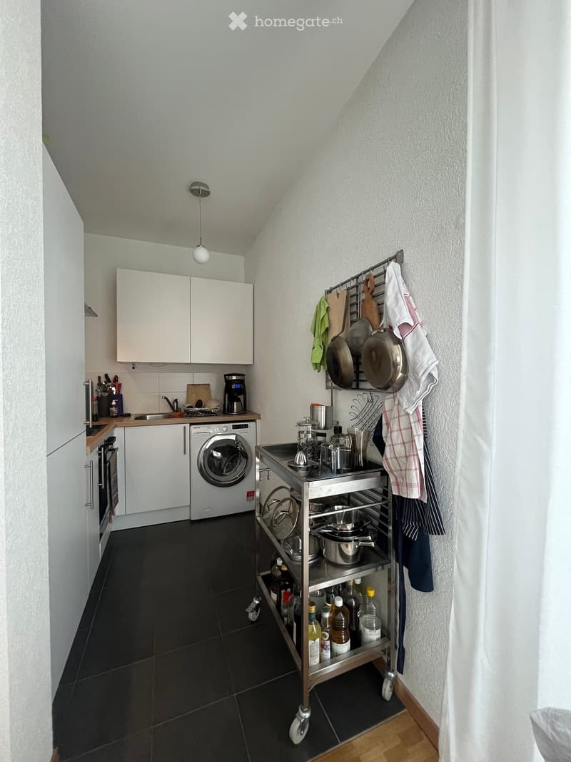Compact kitchen with white cabinets, stainless steel appliances, and a rolling cart holding pots, pans, and utensils.