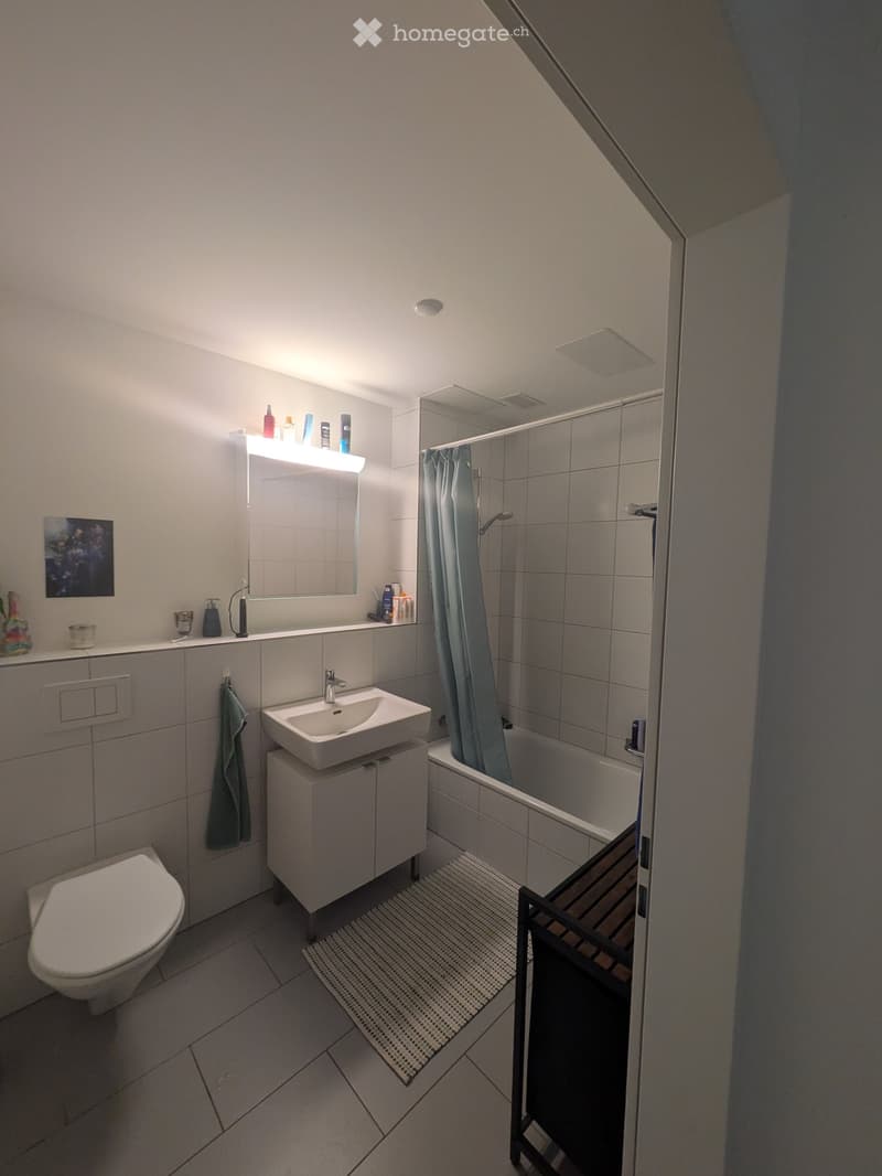 Modern bathroom with a toilet, sink, bathtub, and mirror. Features a built-in cabinet under the sink, a towel hanging on the wall, and a shower curtain in the bathtub area.