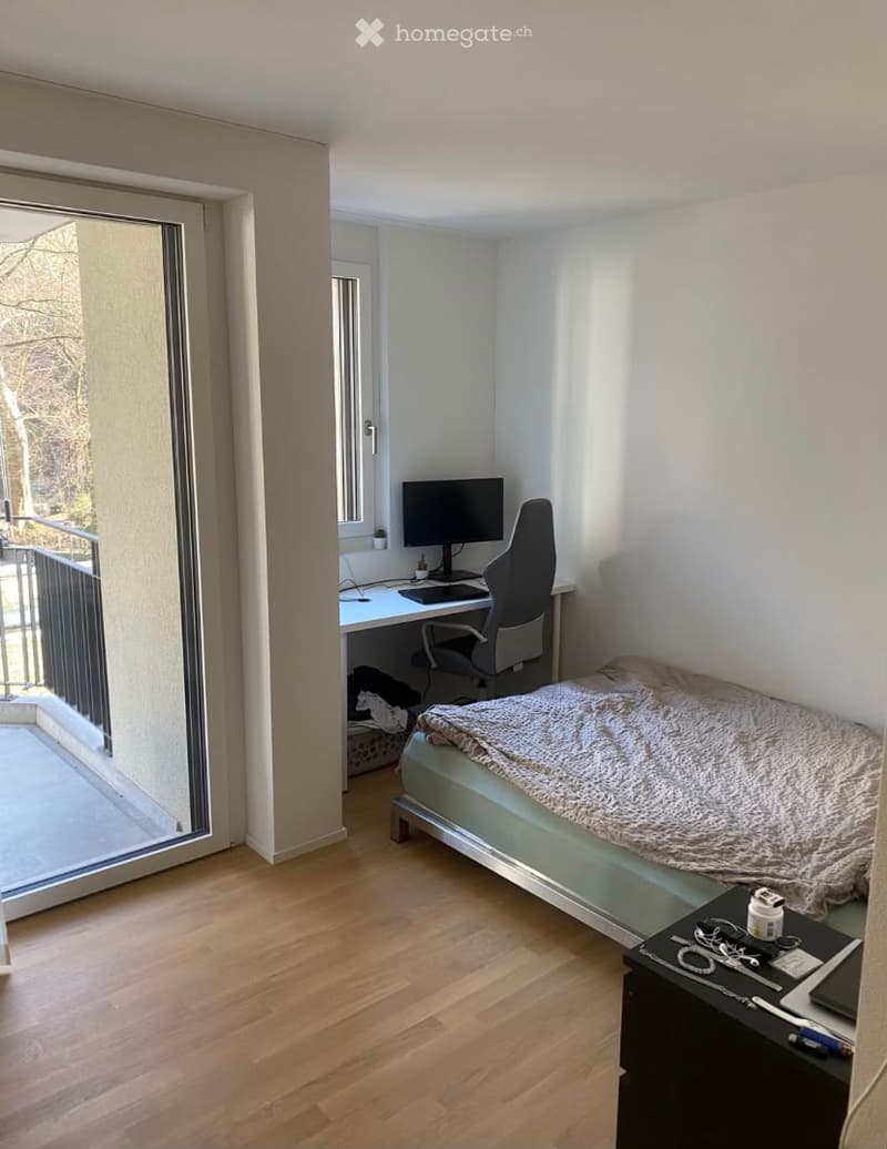 Cozy bedroom with a bed, desk, chair, and laptop. Large window and balcony access.
