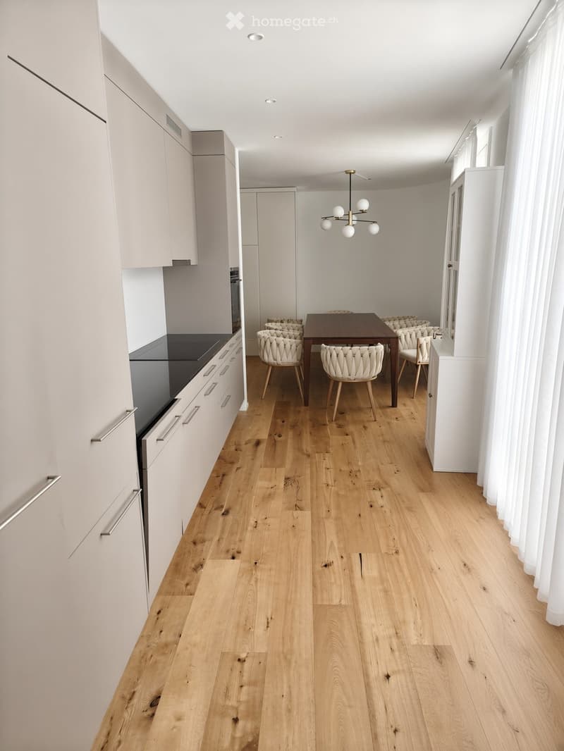 Open-plan kitchen and dining area with light wood flooring, white cabinets, and a modern chandelier.