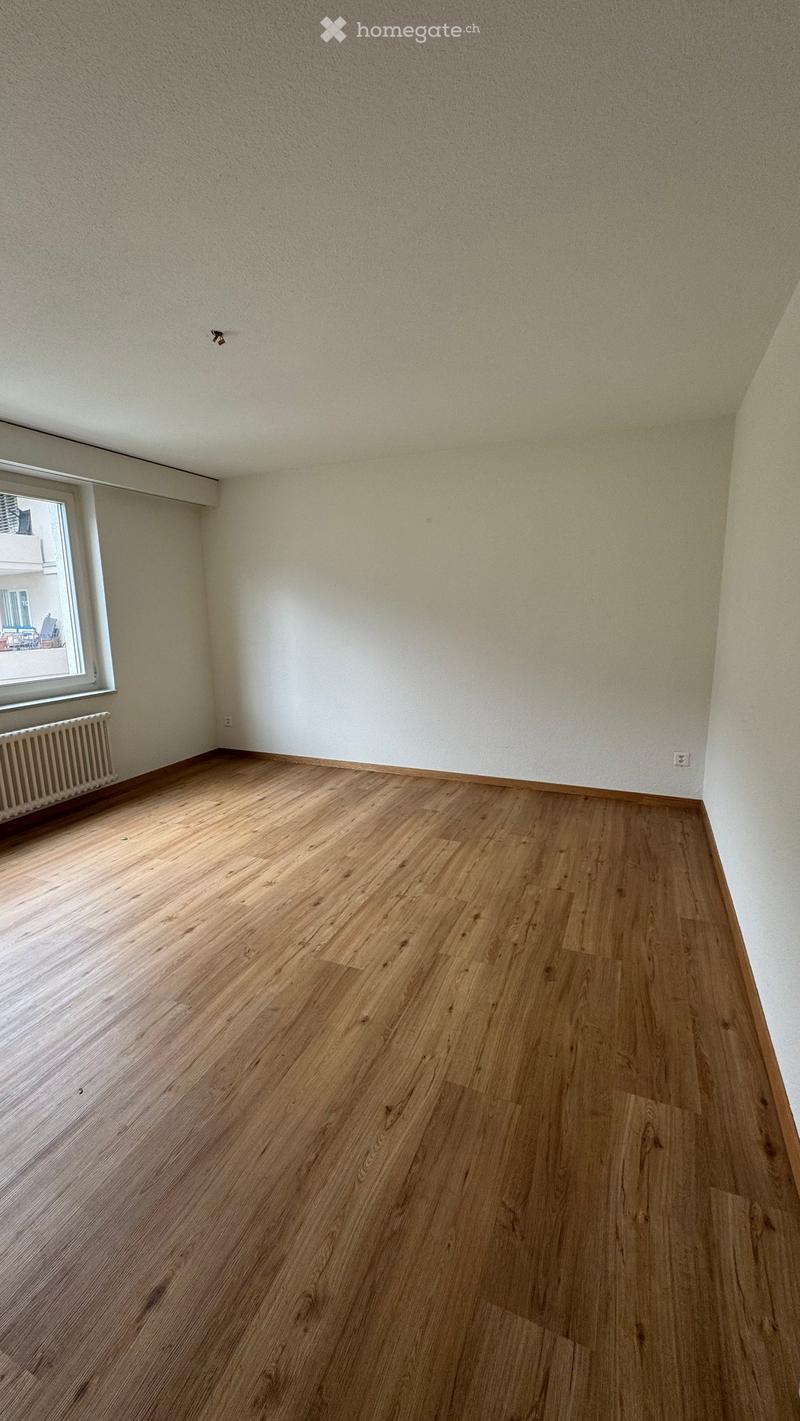 Empty room with wooden flooring, white walls, and a window with a radiator below it.