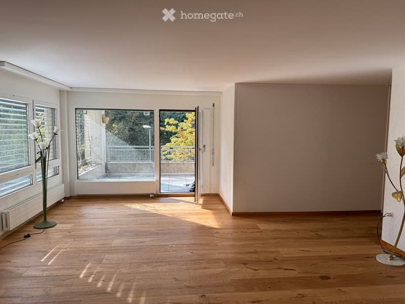 Empty room with wooden flooring, large windows, and a sliding door leading to a balcony.