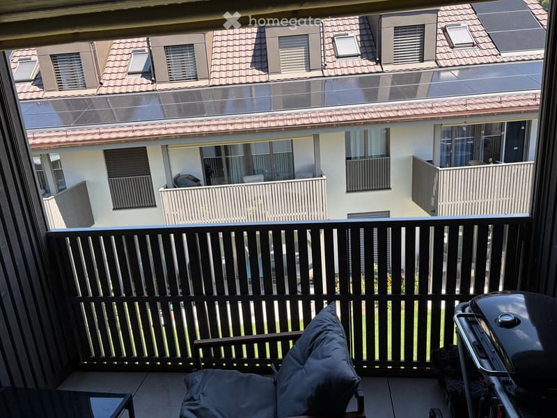 Balcony with a black metal railing, a covered lounge chair, a small table, and a grill in the corner.