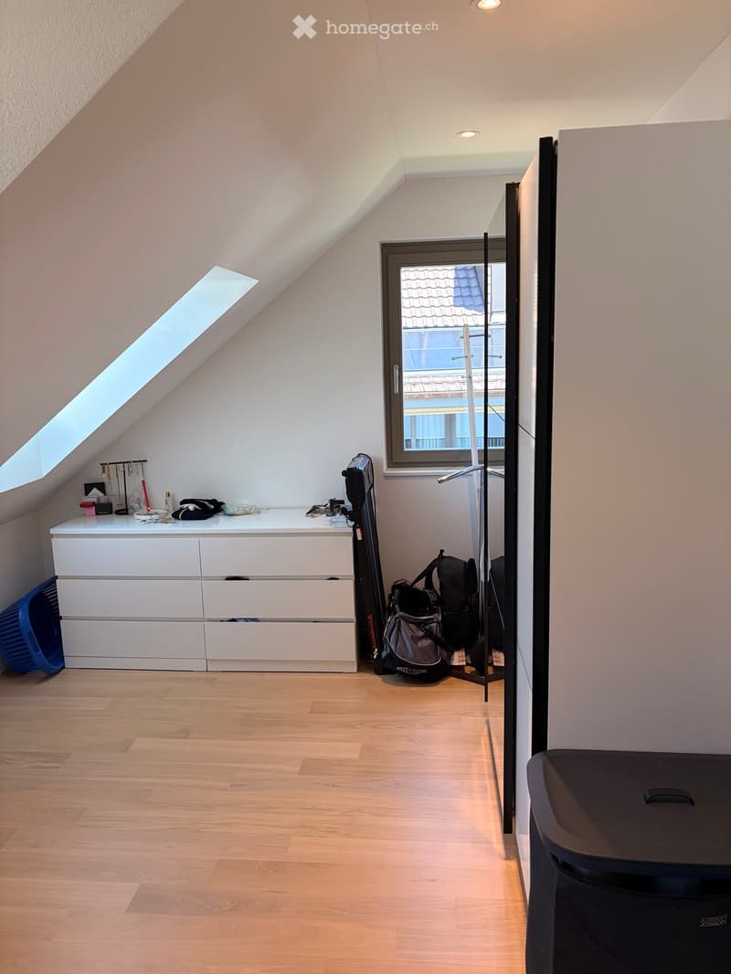 Attic room with wooden flooring, white dresser, window, skylight, and various items including a backpack and guitar.