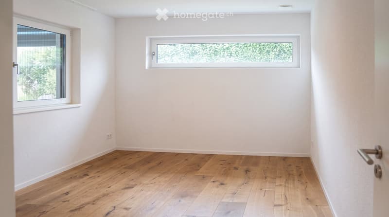 Empty room with light wooden flooring, white walls, and two windows with blinds. No furniture or equipment present.