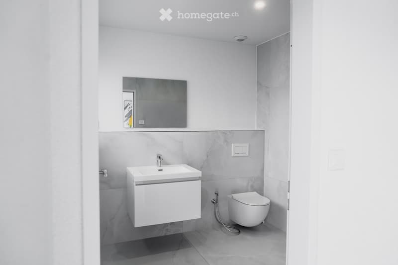 Modern bathroom with white sink, mirror, and toilet, featuring grey marble tiles and sleek fixtures.
