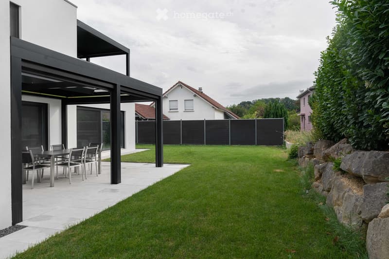 Modern outdoor patio with a covered seating area, a dining table and chairs, a well-maintained lawn, and a stone border.