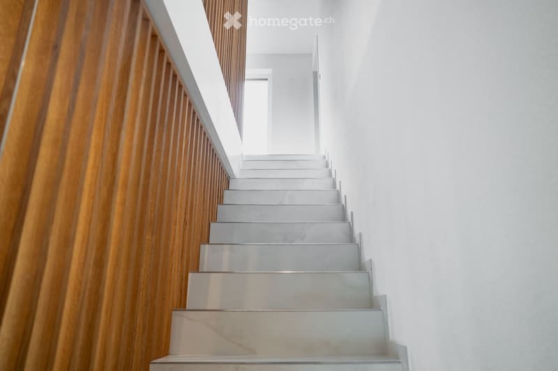 Modern staircase with white marble steps and wooden handrail, leading upwards in a bright, minimalist interior.