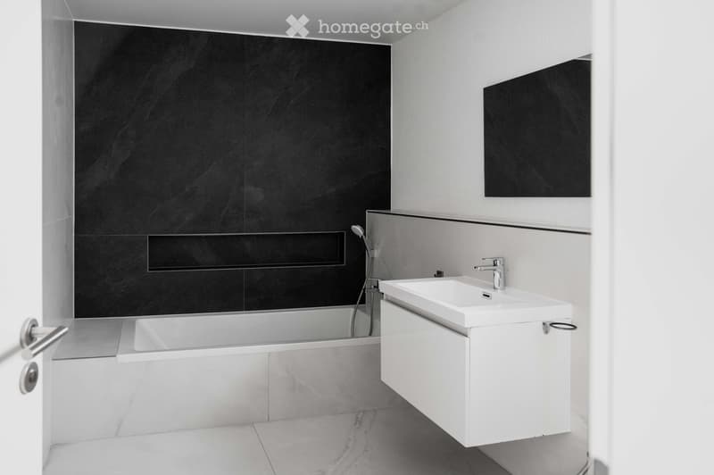 Modern bathroom with a white bathtub, white sink, sleek faucet, and white cabinet. Black marble tiles on the wall and white marble tiles on the floor.