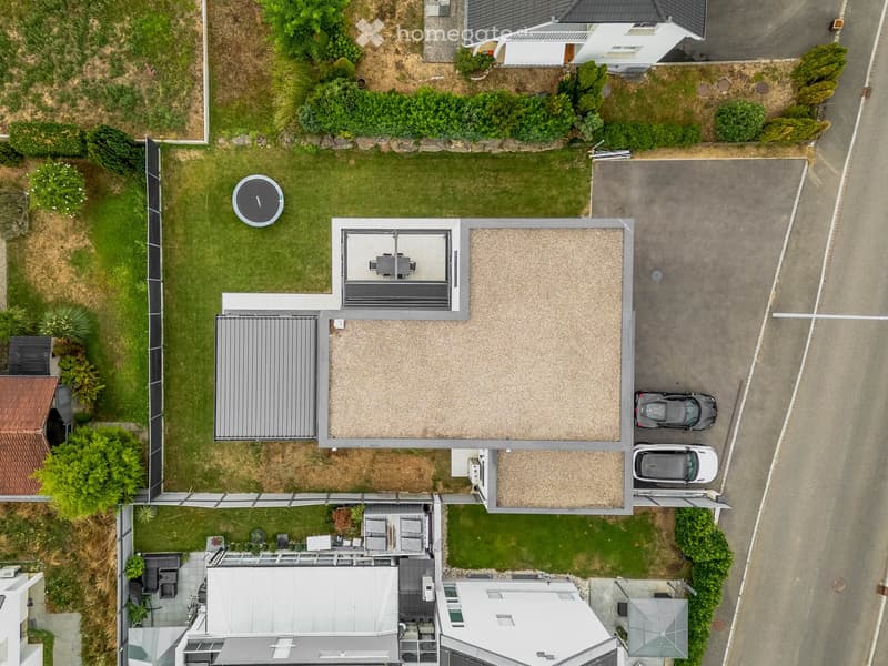 Aerial view of a modern house with a well-maintained garden, patio area, and parking space for two cars.
