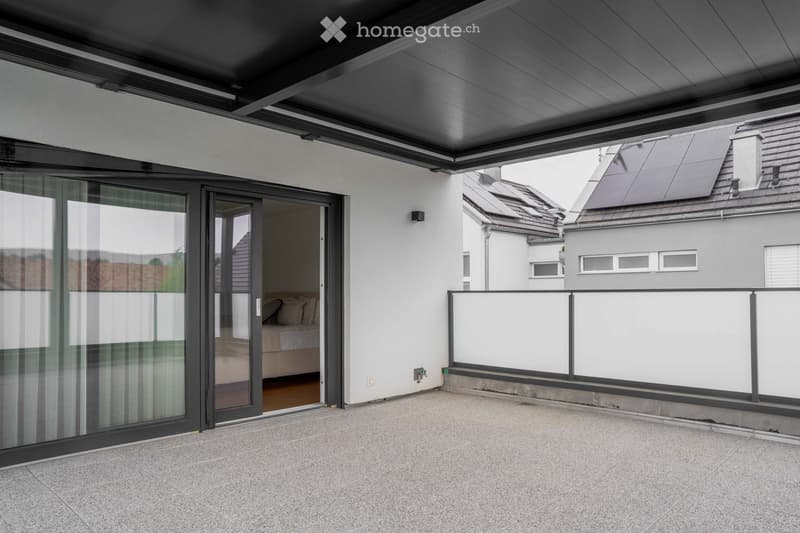 Modern balcony with a sleek, dark grey roof, large glass sliding doors leading to a bedroom, and a white railing with a clean, minimalist design.