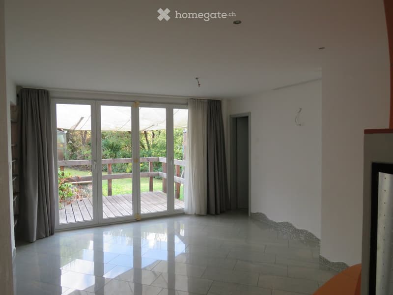 Empty room with large sliding glass doors leading to a wooden deck, white tiled floor, and light-colored walls.