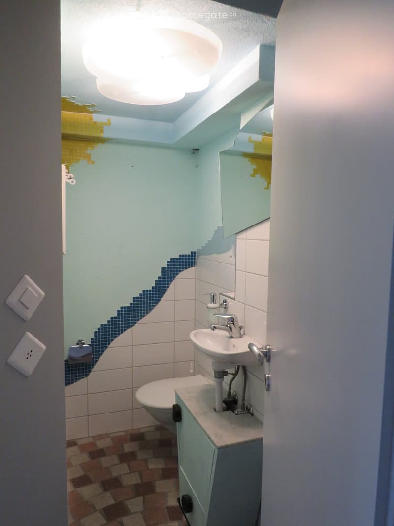 Modern bathroom with a sink, mirror, toilet, and cabinet. Light blue walls with a decorative blue tile accent, and a unique cloud-shaped light fixture on the ceiling.