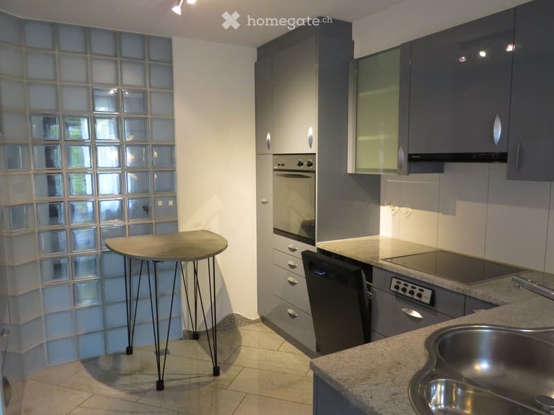 Modern kitchen with grey cabinets, stainless steel appliances, granite countertop, and a small round table.