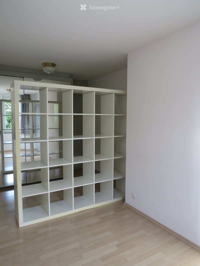 Empty room with light wooden flooring, white walls, and a large white shelving unit with multiple compartments and shelves.