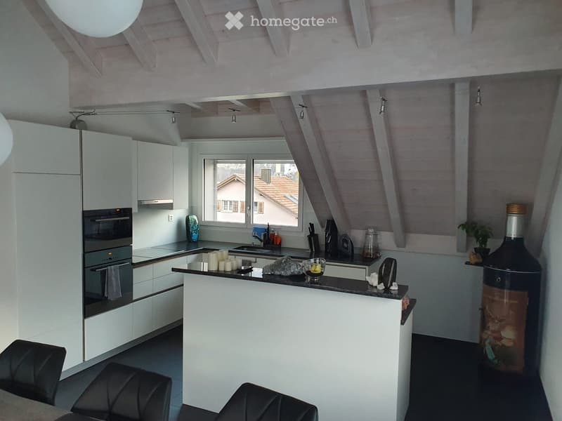 Modern kitchen with white cabinets, black countertops, and a central island. Features an oven, sink, and decorative items including candles and a large bottle.