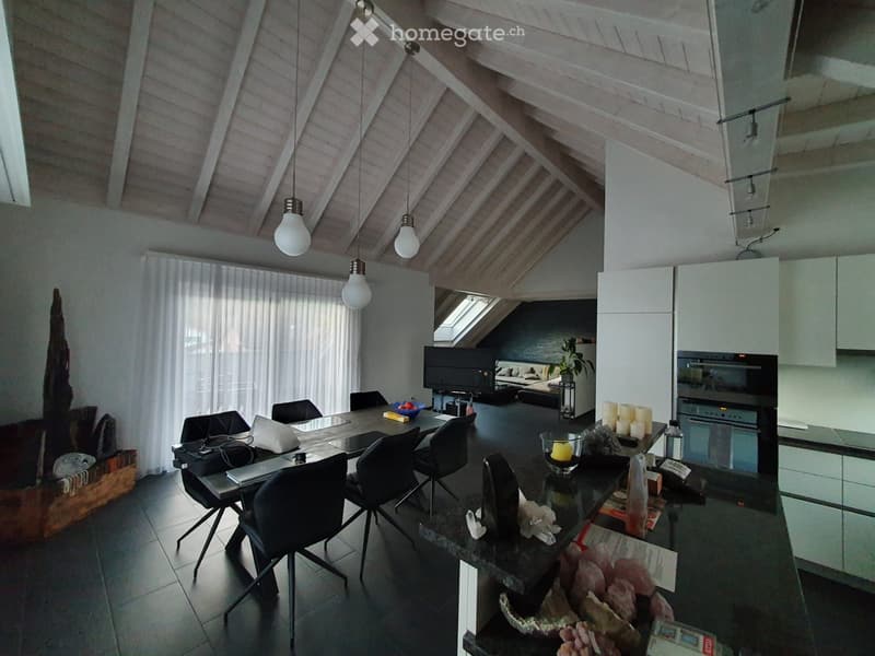 Open-plan living and dining area with a modern kitchen, featuring a dining table with chairs, a laptop, candles, and a television in the background.
