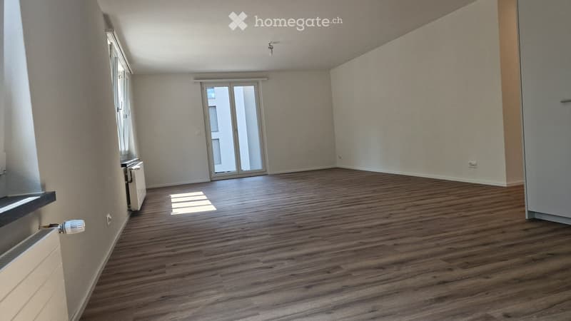 Empty room with wooden flooring, large sliding glass door, and radiator on the wall.