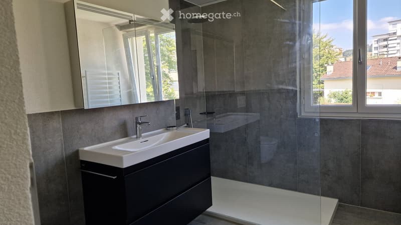 Modern bathroom with a white sink, black cabinet, glass shower enclosure, and large windows offering a view of the city.
