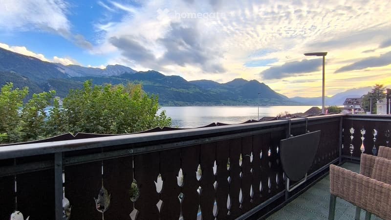 Balcony with wooden railing overlooking a scenic lake and mountain view.
